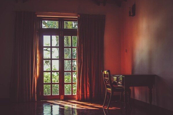 A room with a large window, curtains, a chair, and a small table.