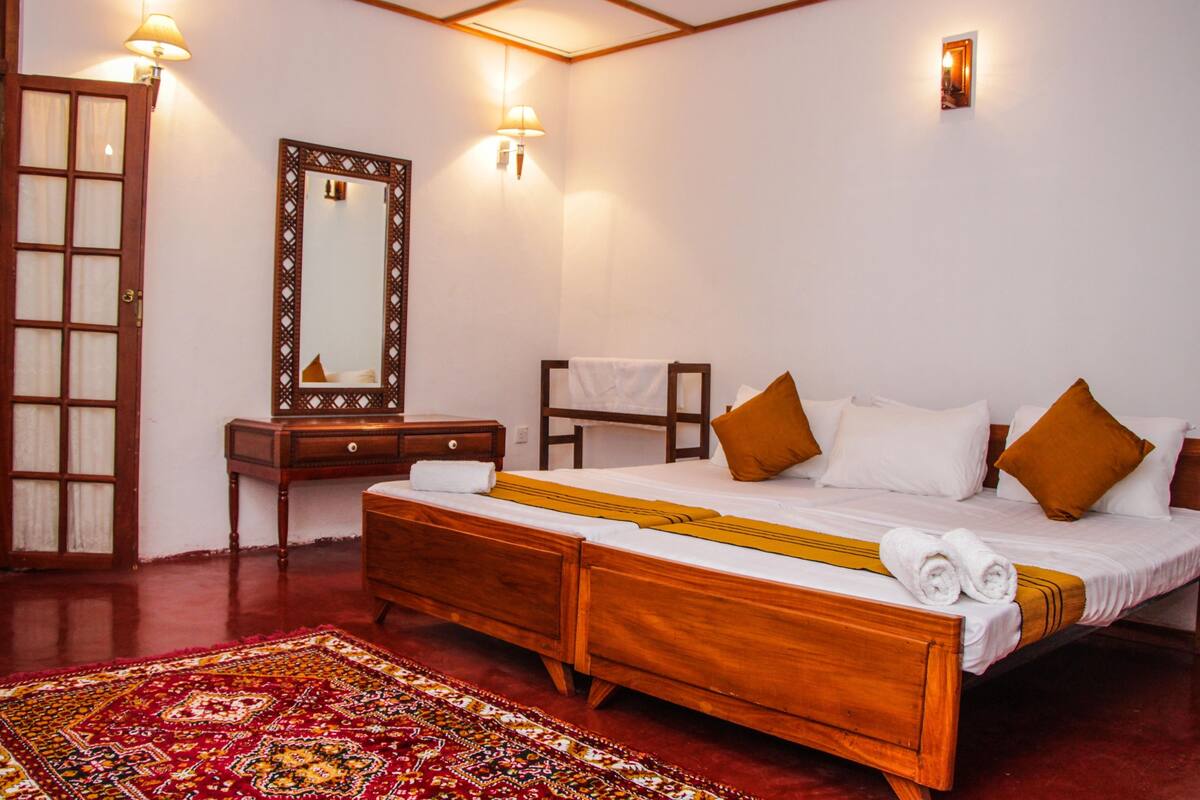 A traditional wooden bed with white and brown pillows, a wooden nightstand, a mirror, and a red patterned rug.