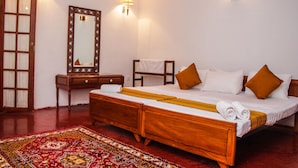 Una cama de madera tradicional con almohadas blancas y marrones, una mesita de noche de madera, un espejo y un tapete rojo con estampado.