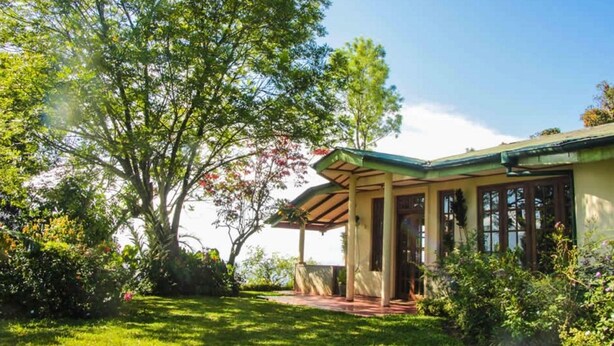 Una casa con porche cubierto, rodeada de abundante vegetación y árboles.