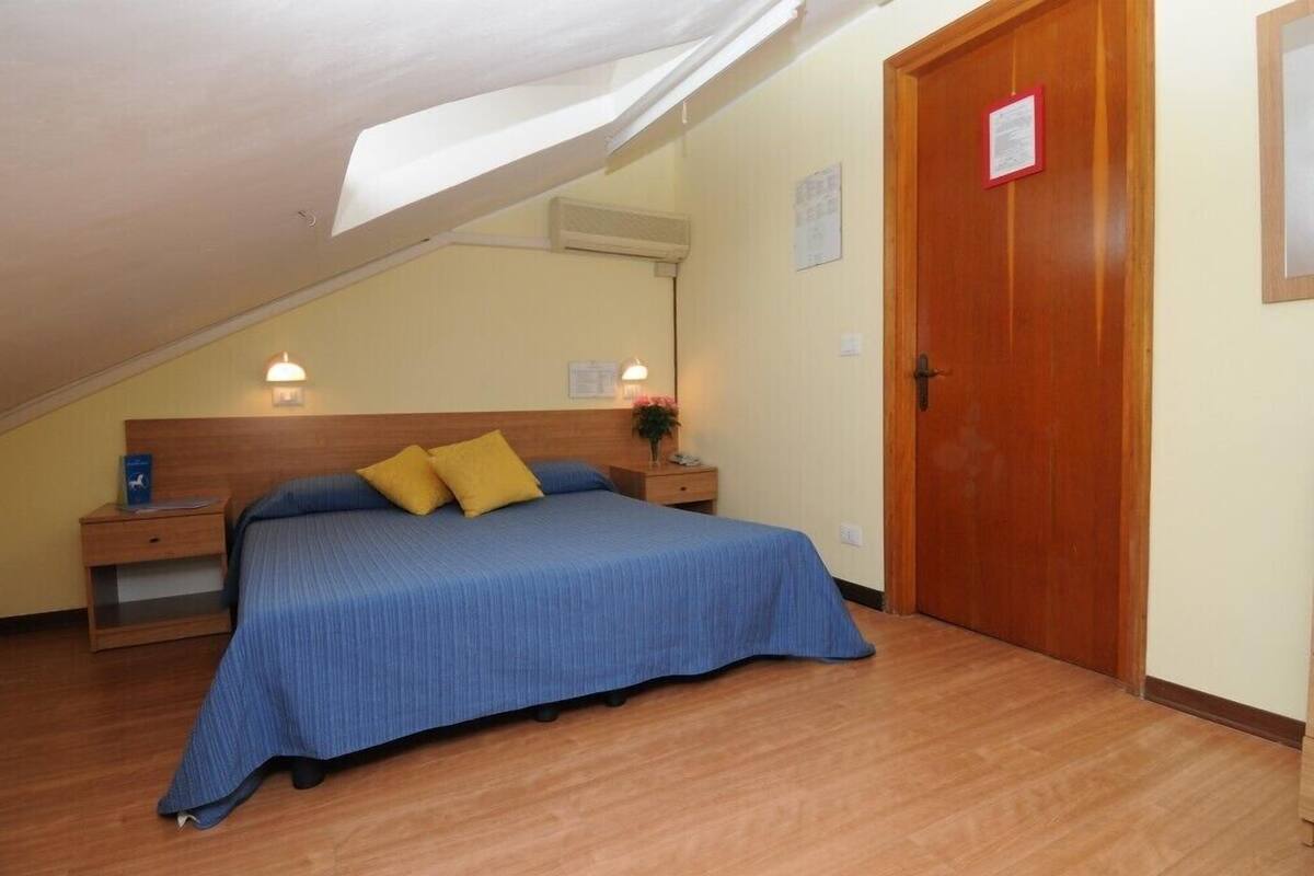 Une chambre avec un lit simple, une tête de lit en bois, des tables de chevet et une porte en bois.