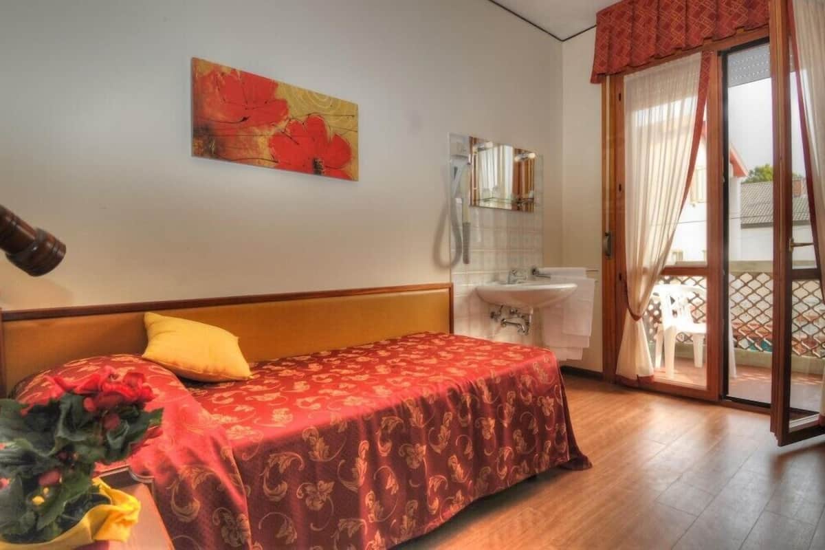Une chambre à coucher comprenant un lit, une table de chevet, un miroir, un lavabo et une porte-fenêtre coulissante donnant sur un espace extérieur.