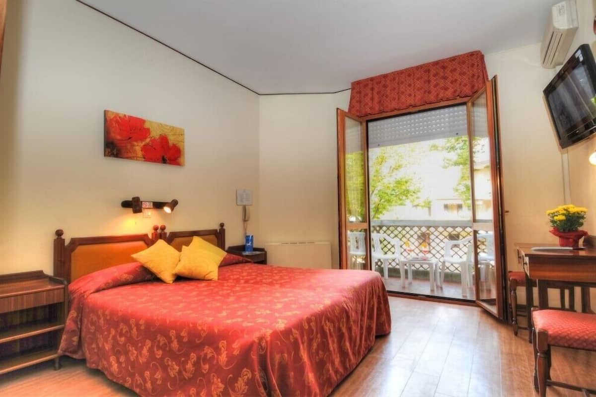 Une chambre d’hôtel avec un lit, un bureau, une chaise, un balcon avec vue et un tableau au mur.