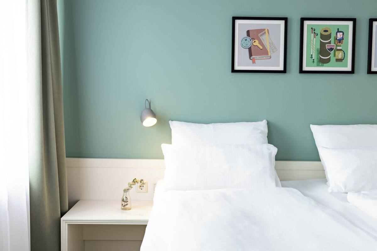 A neatly made bed in a room with teal walls, a bedside lamp, and two framed pictures on the wall.