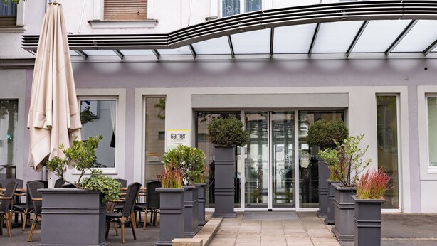 A hotel entrance with a covered patio area, outdoor seating, and potted plants.