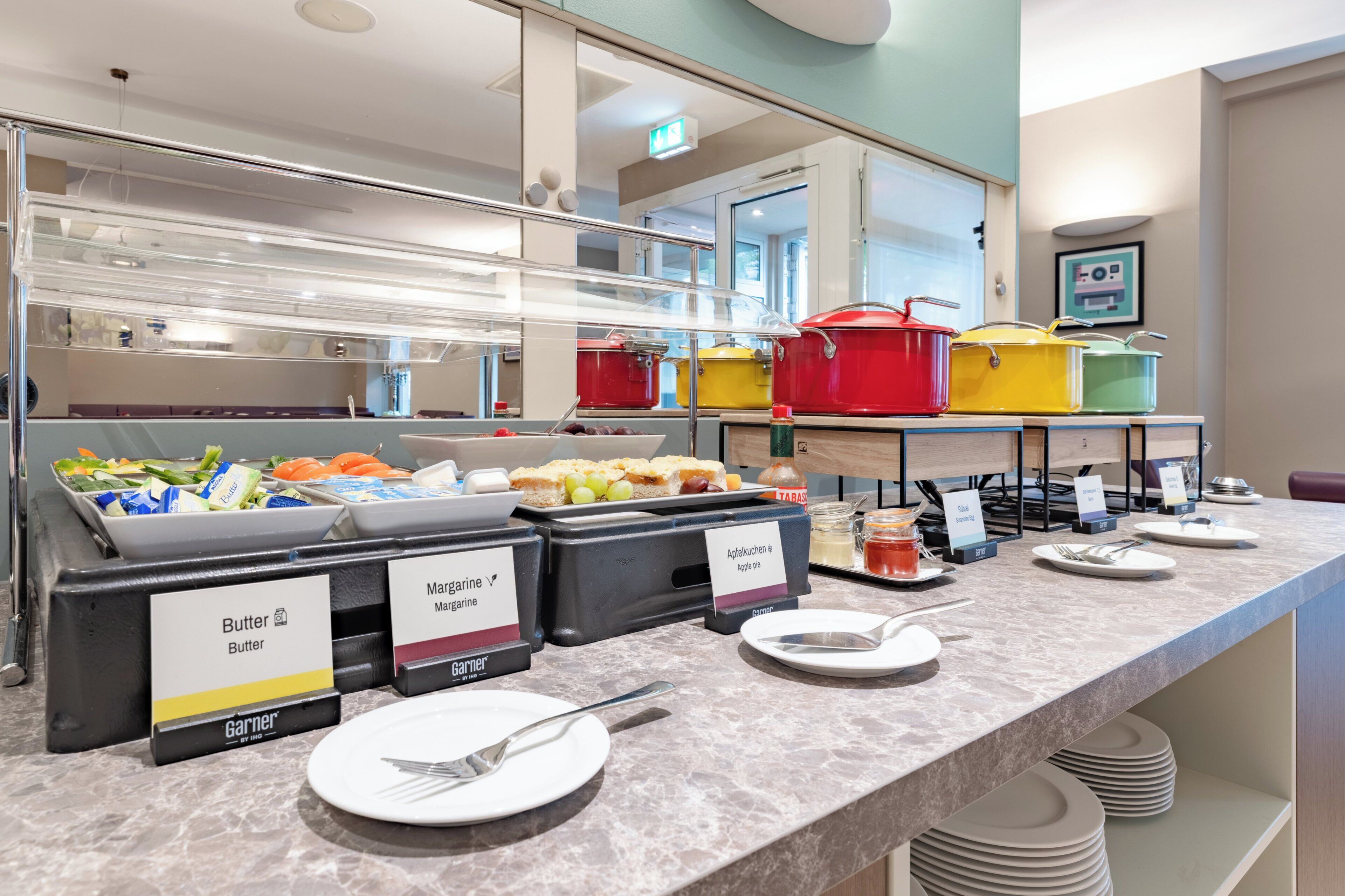 Zona de buffet con estaciones de comida identificadas, incluyendo mantequilla, margarina y tarta de manzana.