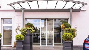 A hotel entrance with a covered walkway, glass doors, and potted plants.
