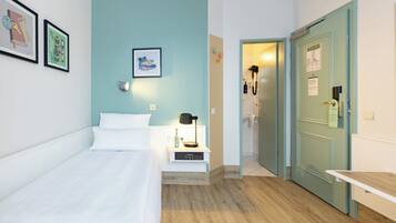Une chambre comprenant un lit, une table de chevet, une lampe fixée au mur et une porte donnant accès à une salle de bain.