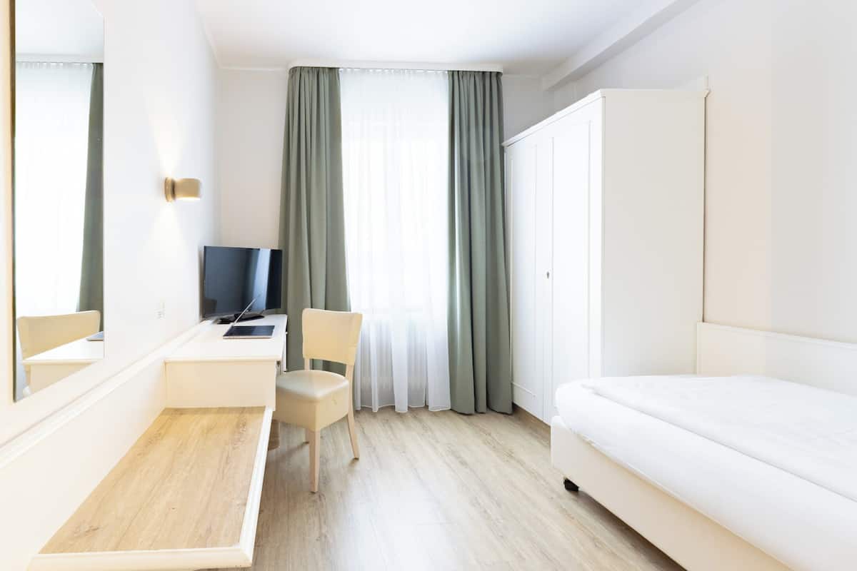 A hotel room with a bed, a desk with a chair, a television, and a large mirror.