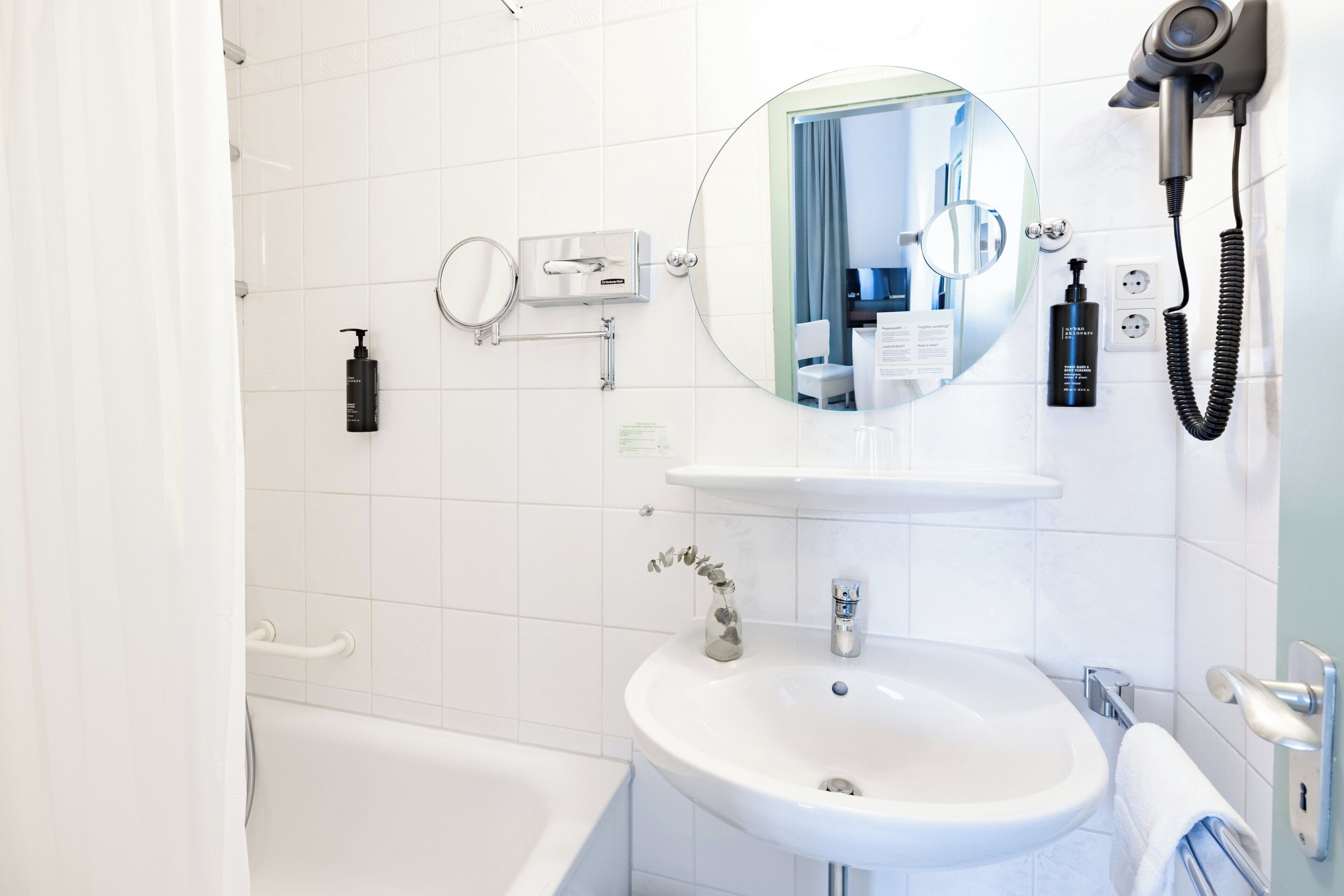 Un baño con lavamanos blanco, espejo y secador de pelo fijado en la pared.