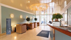 A modern lobby with a reception desk, seating area, and a large chandelier.