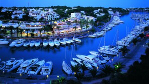 A marina with numerous boats docked, a waterfront promenade, and buildings with outdoor seating areas.