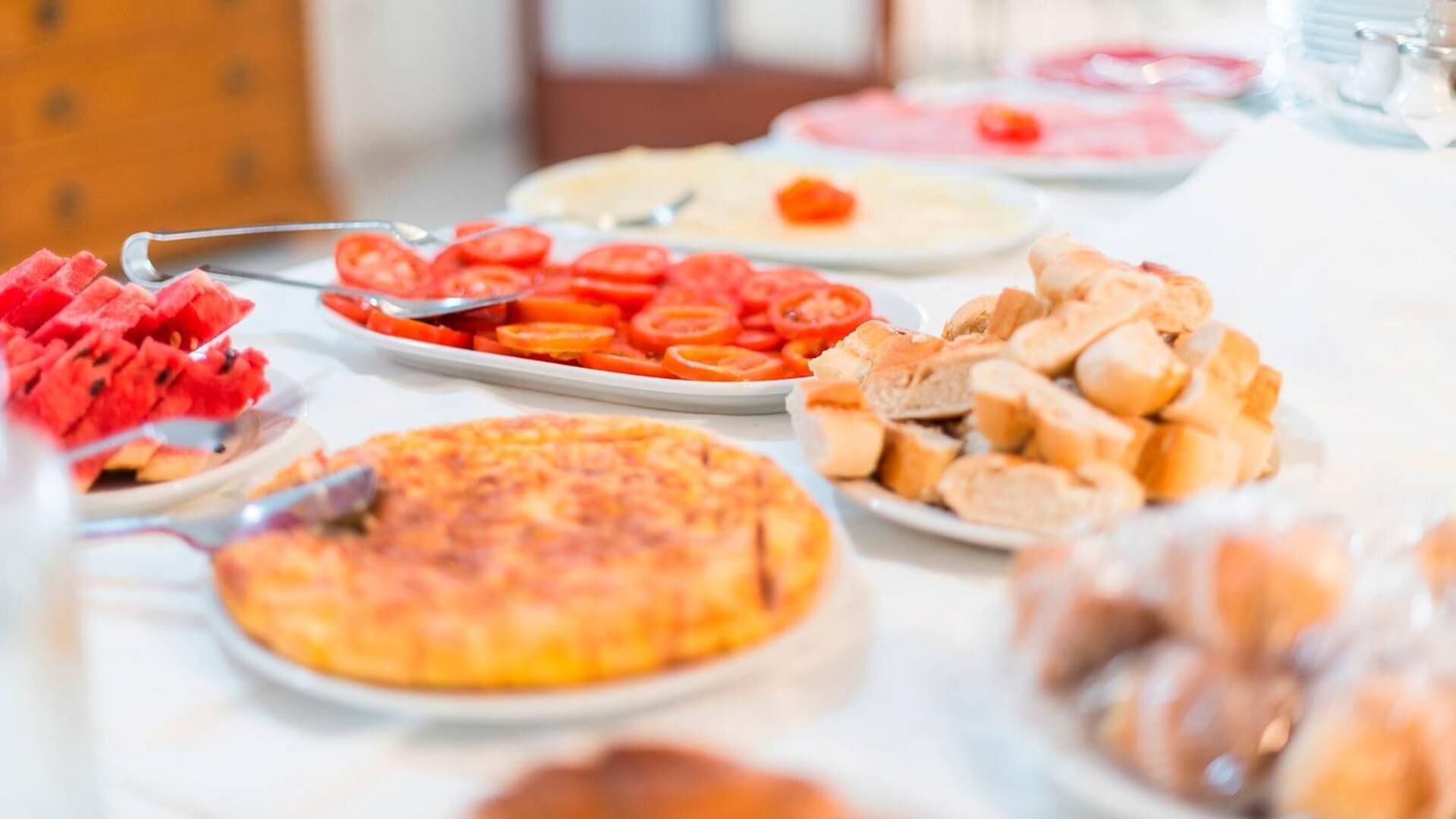 Una mesa de bufé con diferentes opciones de comida, incluyendo sandía, rodajas de tomate, pan y pizza.