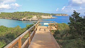 A wooden boardwalk leading to a coastal area with rocky cliffs and clear blue waters.