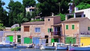 A coastal village with traditional stone buildings, boats docked at the harbor, and lush greenery in the background.