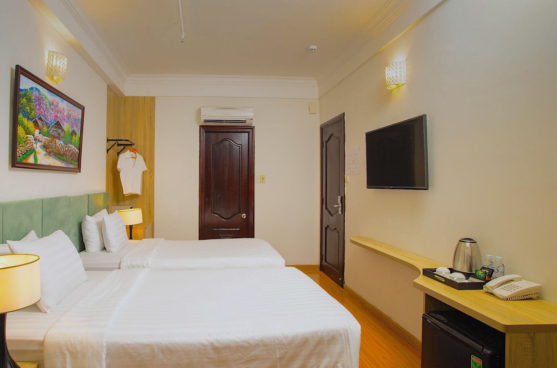 A hotel room with two beds, a TV, a desk with a phone and coffee maker, and a painting on the wall.
