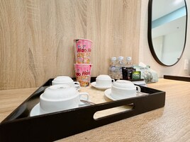 A tray with white cups and saucers, a stack of pink and white containers, and a tray of bottled water and tea bags.