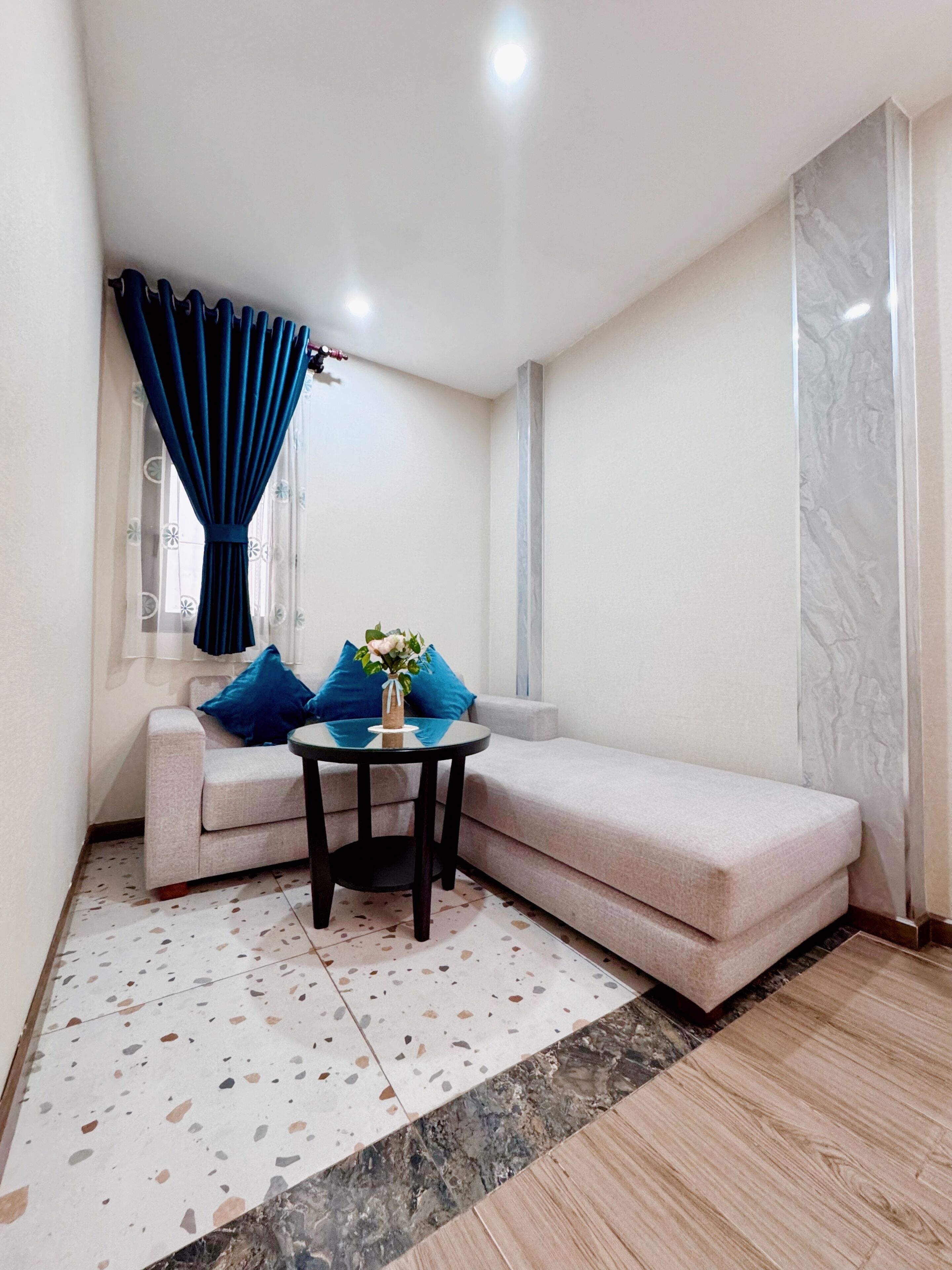 A corner room with a sofa, a small round table, and a window with blue curtains.
