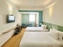A hotel room with two beds, a desk, a chair, a television, and a window with curtains.