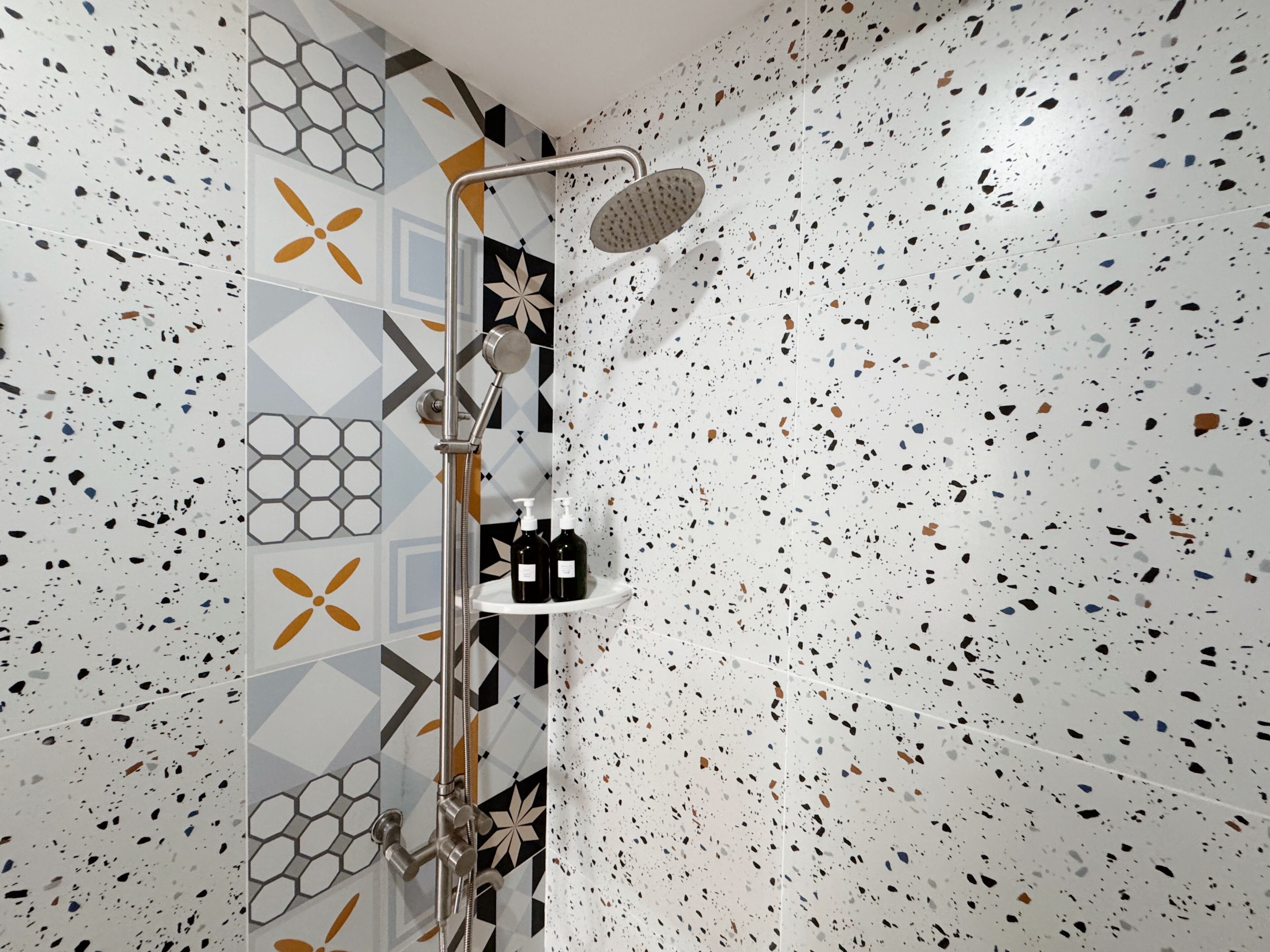 A shower with a handheld showerhead and a wall-mounted control panel.