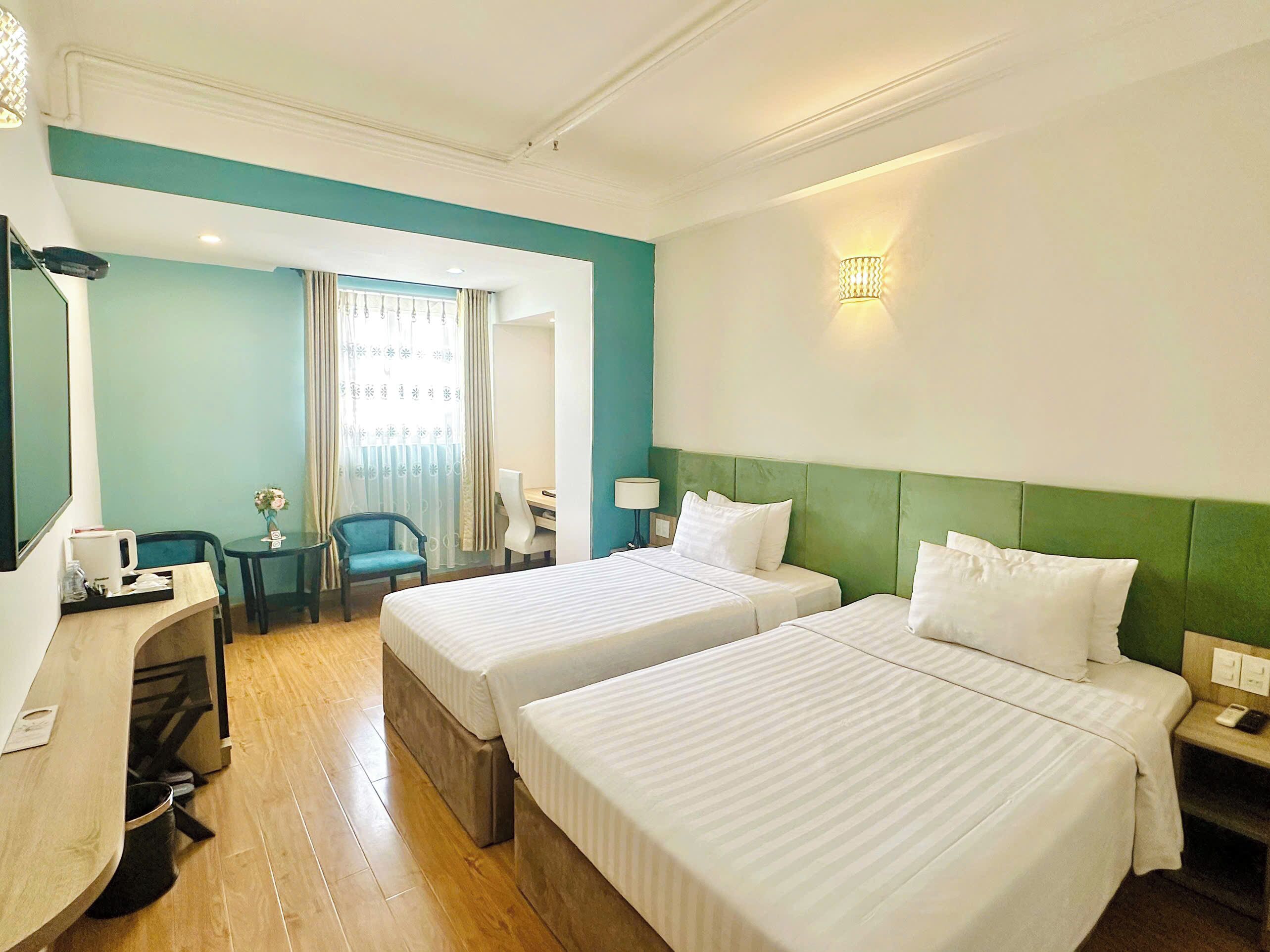 A hotel room with two beds, a desk, a chair, and a window with curtains.