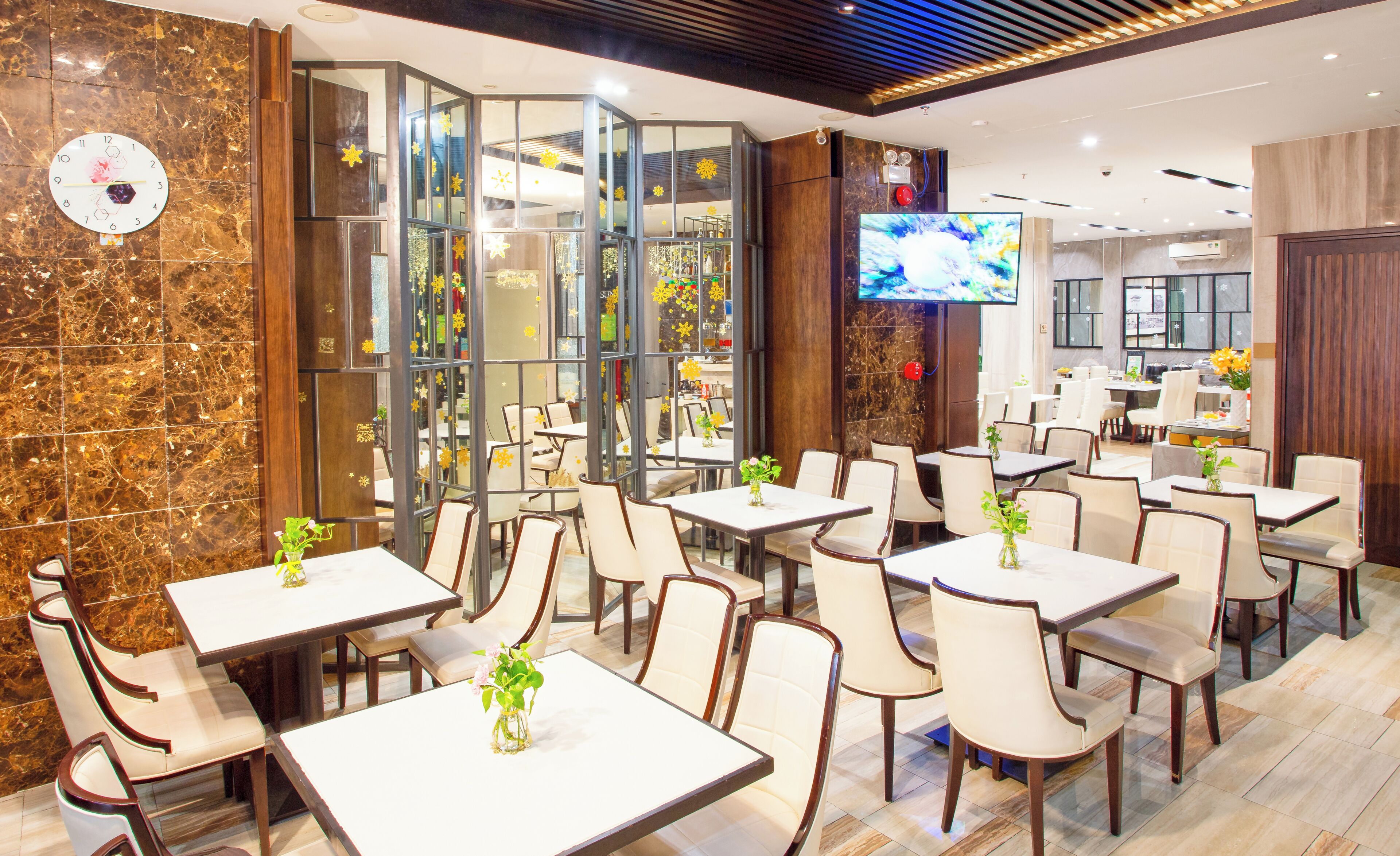 Ein Restaurant mit mehreren Tischen und Stühlen, einer Uhr an der Wand und einem Fernsehbildschirm.