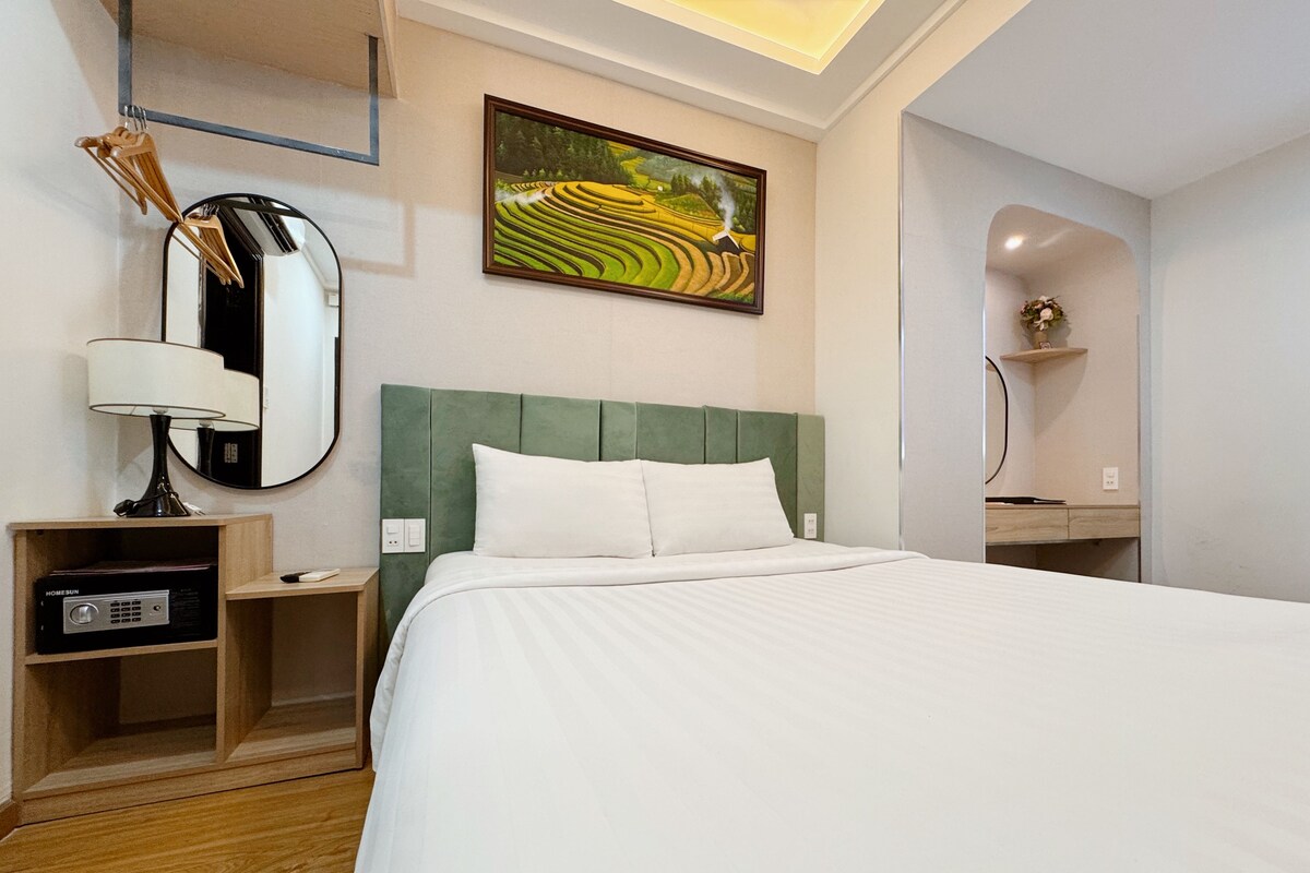 Une chambre d’hôtel avec un grand lit, une table de chevet, une lampe, un miroir et un tableau au mur.