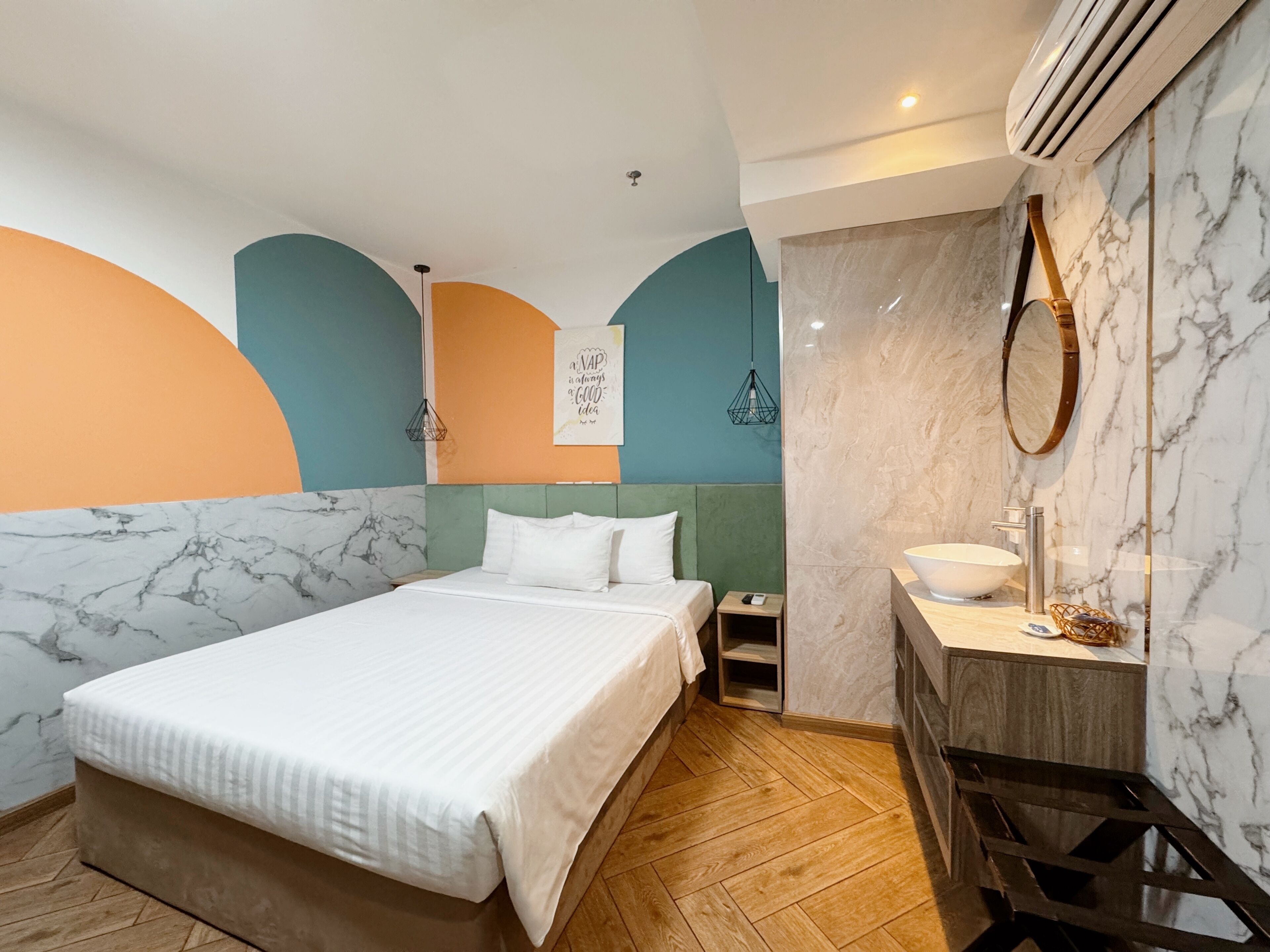 A modern hotel room with a bed, bedside table, and a bathroom with a sink and mirror.