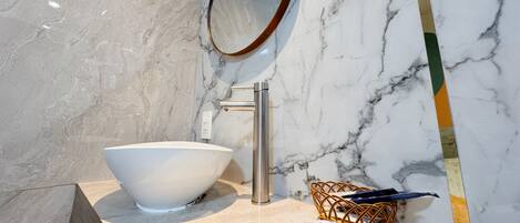 A bathroom with a white marble sink, a chrome faucet, a round mirror, and a wicker basket on the countertop.