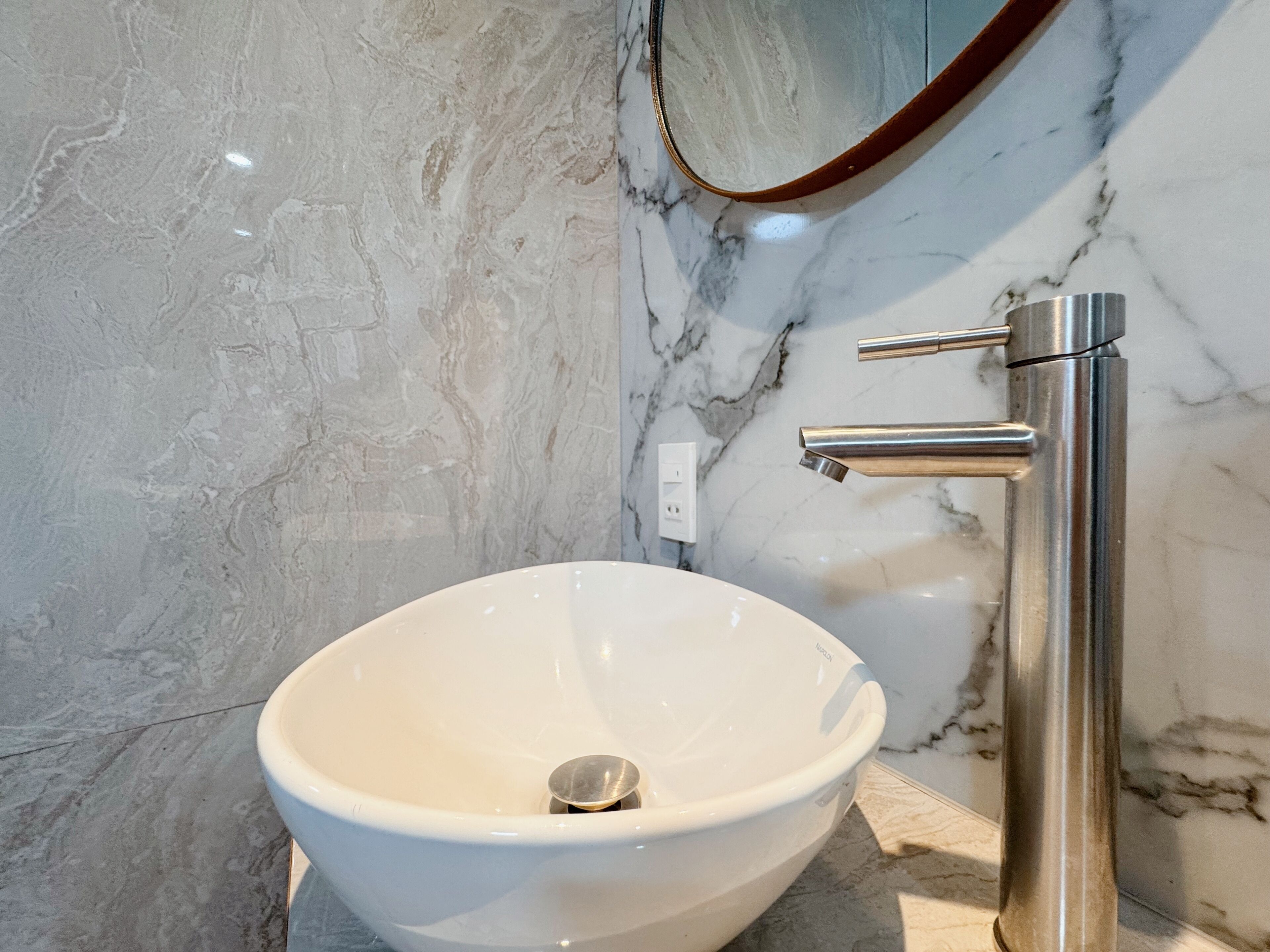 A bathroom with a white ceramic sink, a chrome faucet, and a marble wall.