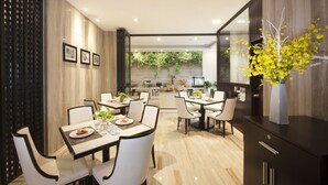 A modern dining area with a kitchen in the background, featuring a dining table with chairs, a vase with yellow flowers, and framed pictures on the wall. - Sunrise Central Hotel (Ho Chi Minh City)