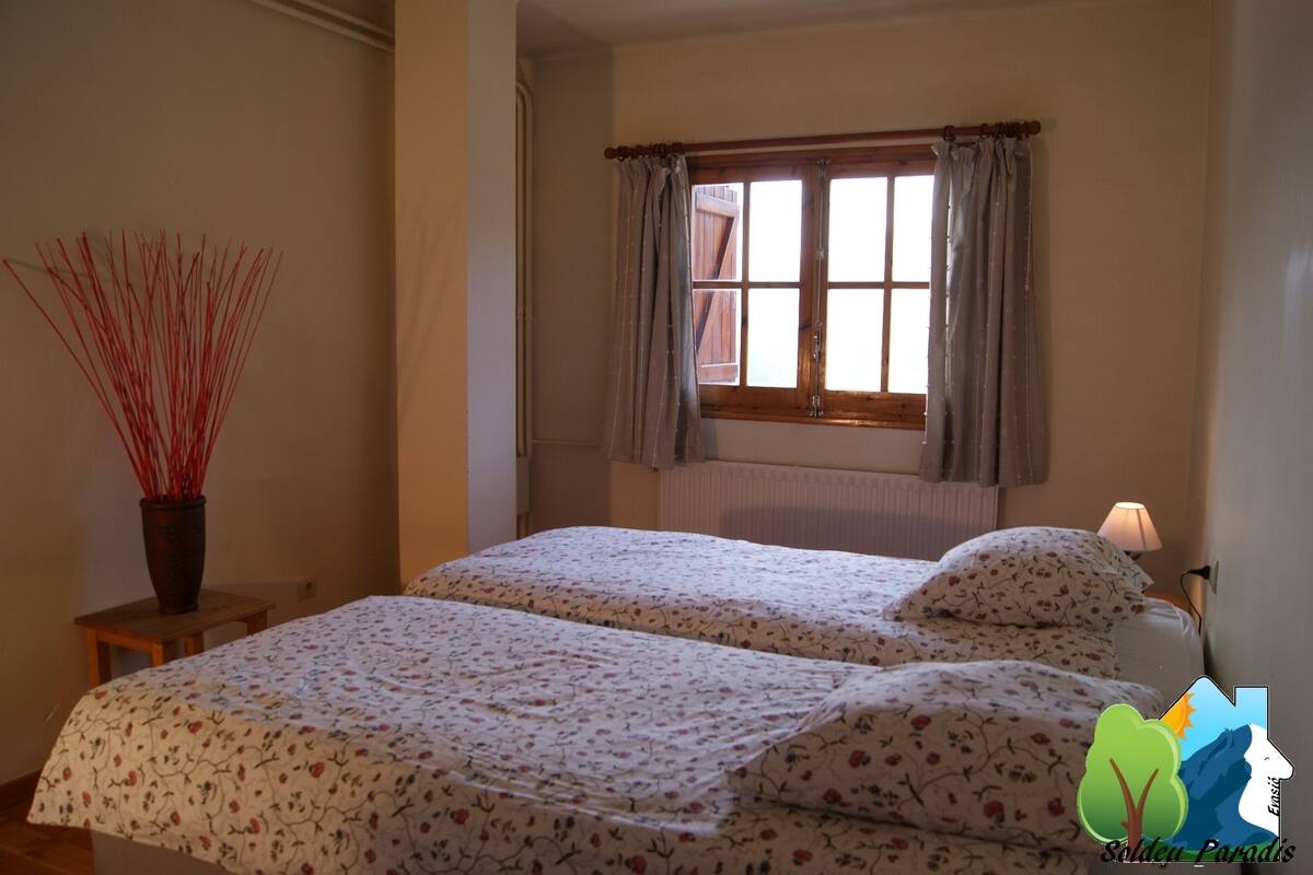 Un dormitorio con dos camas, una ventana con cortinas, un radiador y una lámpara sobre una mesita de noche.