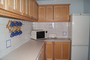A kitchen with wooden cabinets, a microwave, a toaster, and a refrigerator. - Soldeu Paradis (Soldeu)