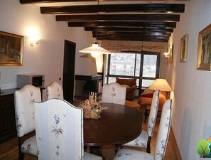 A dining area with a round table, floral-upholstered chairs, a fireplace, and a large window providing a view. - Soldeu Paradis (Soldeu)