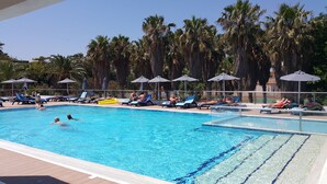 A swimming pool with lounge chairs and umbrellas, surrounded by palm trees. - Cosmopolitan Kos Hotel (Kos)