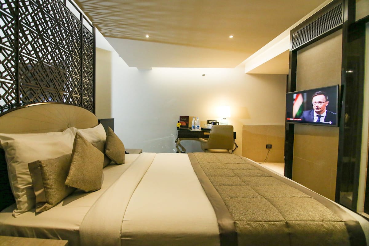 Habitación de hotel con cama, escritorio, televisor y un panel decorativo.