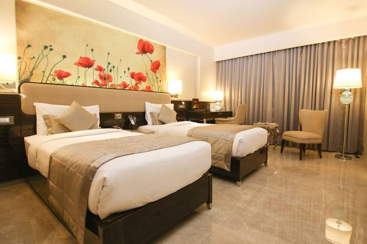 Habitación de hotel con dos camas, un escritorio, una silla, un cuadro en la pared y un ventanal con cortinas.