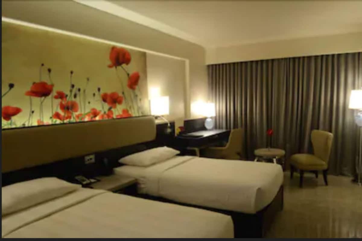 Habitación de hotel con dos camas, un escritorio, una silla y una gran obra de arte floral en la pared.