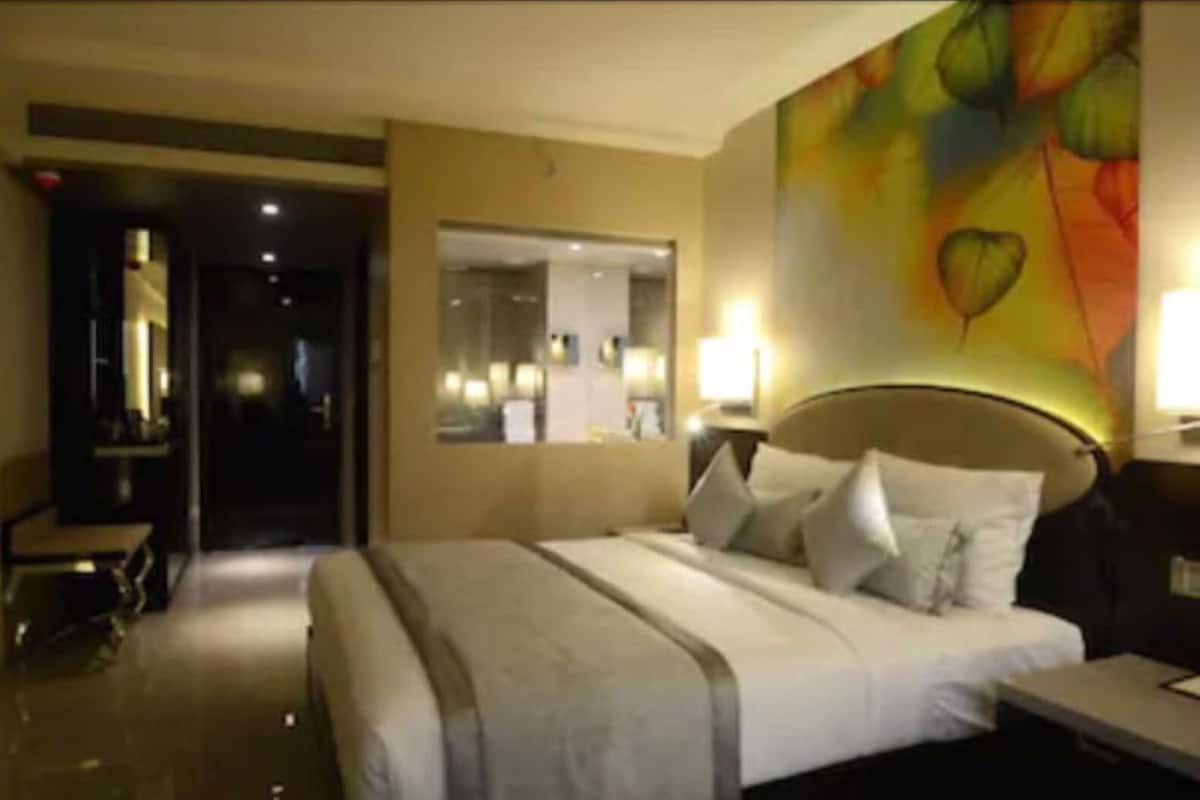 Una habitación de hotel con cama, mesita de noche, lámpara y espejo.