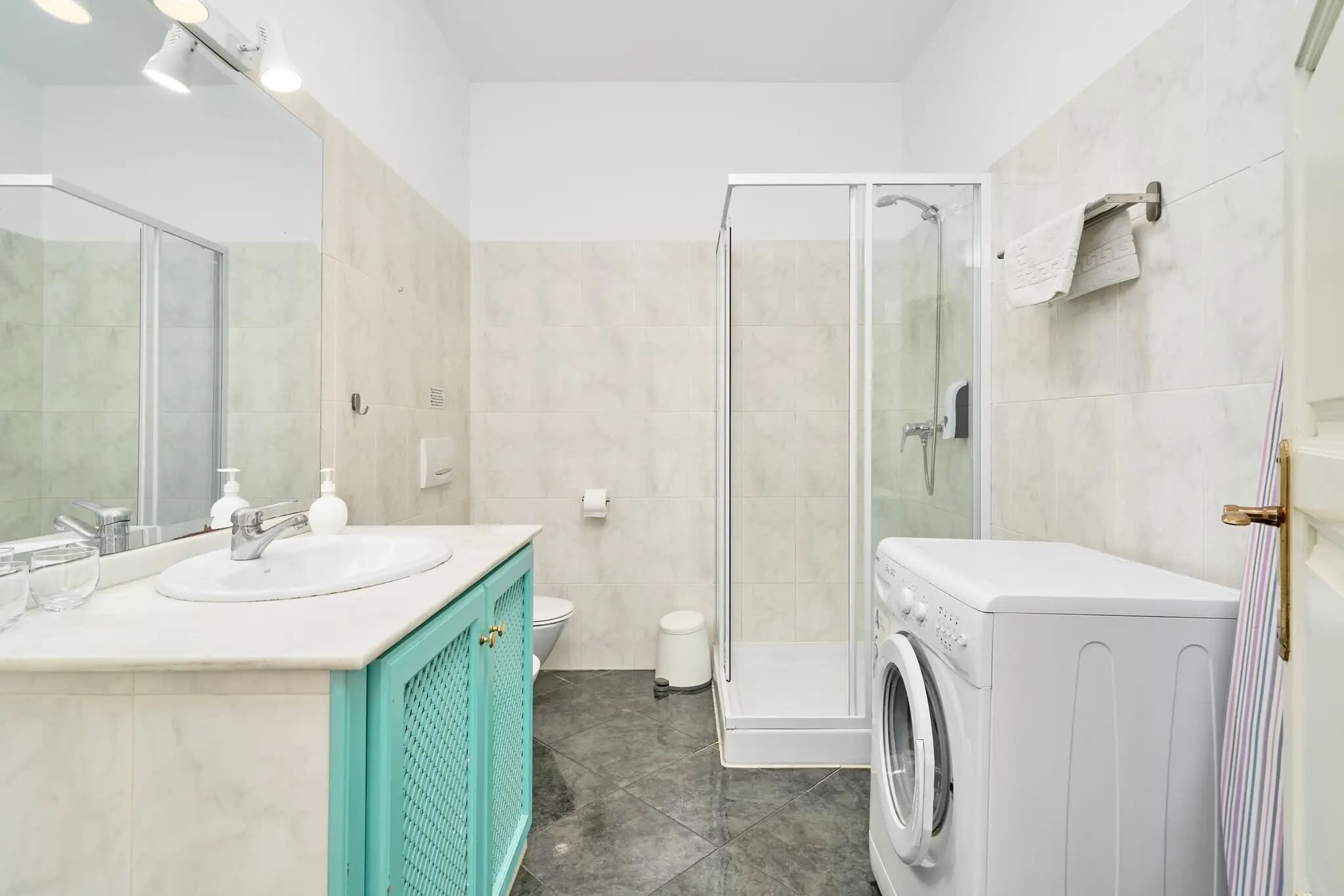Un baño moderno con cabina de ducha de vidrio, lavadora y mueble de tocador doble.