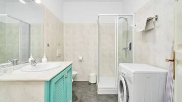 Un baño moderno con cabina de ducha de vidrio, lavadora y mueble de tocador doble.