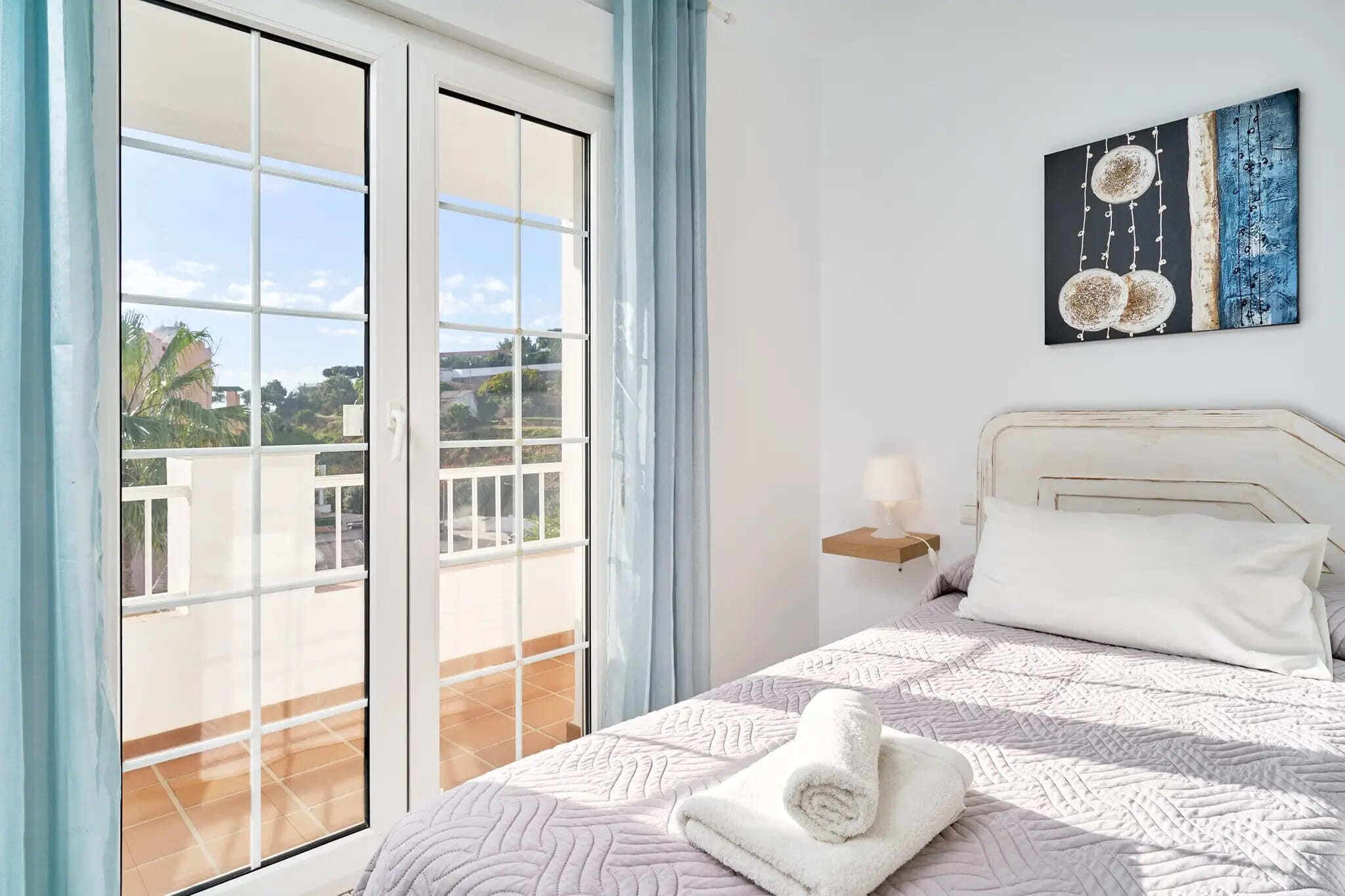 Une chambre à coucher avec un lit, un tableau, une fenêtre donnant sur un paysage et un rideau.