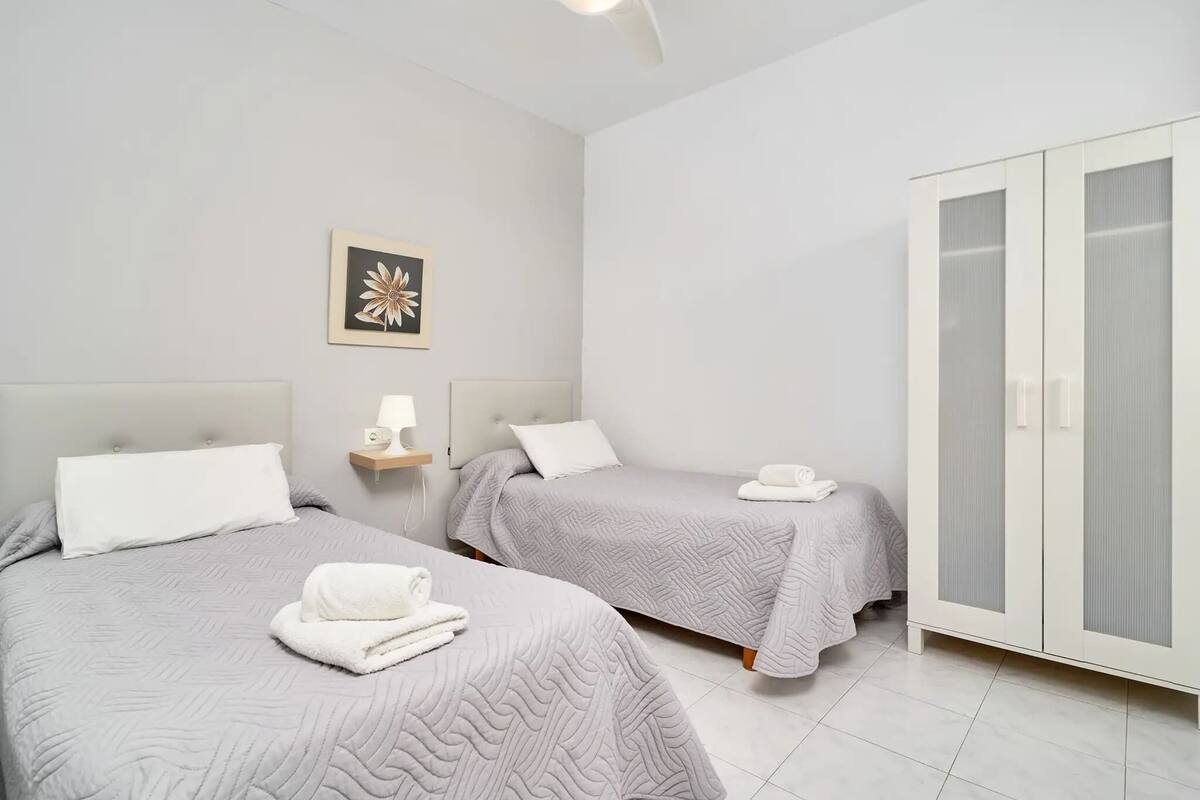 A hotel room with two beds, a wardrobe, a wall-mounted lamp, and a framed picture.