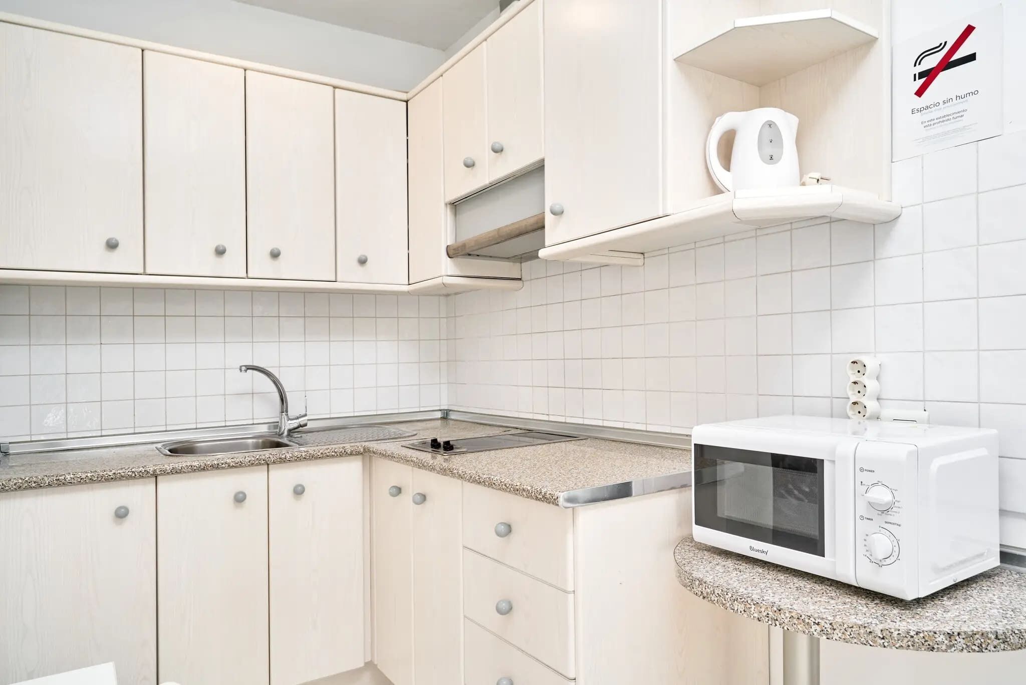 A kitchen with white cabinets, a microwave, and a kettle on a countertop.