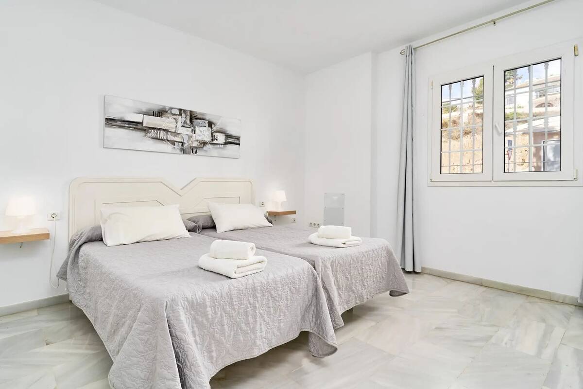 A double room with two beds, a window with a view, a wall-mounted artwork, and a bedside table with a lamp.