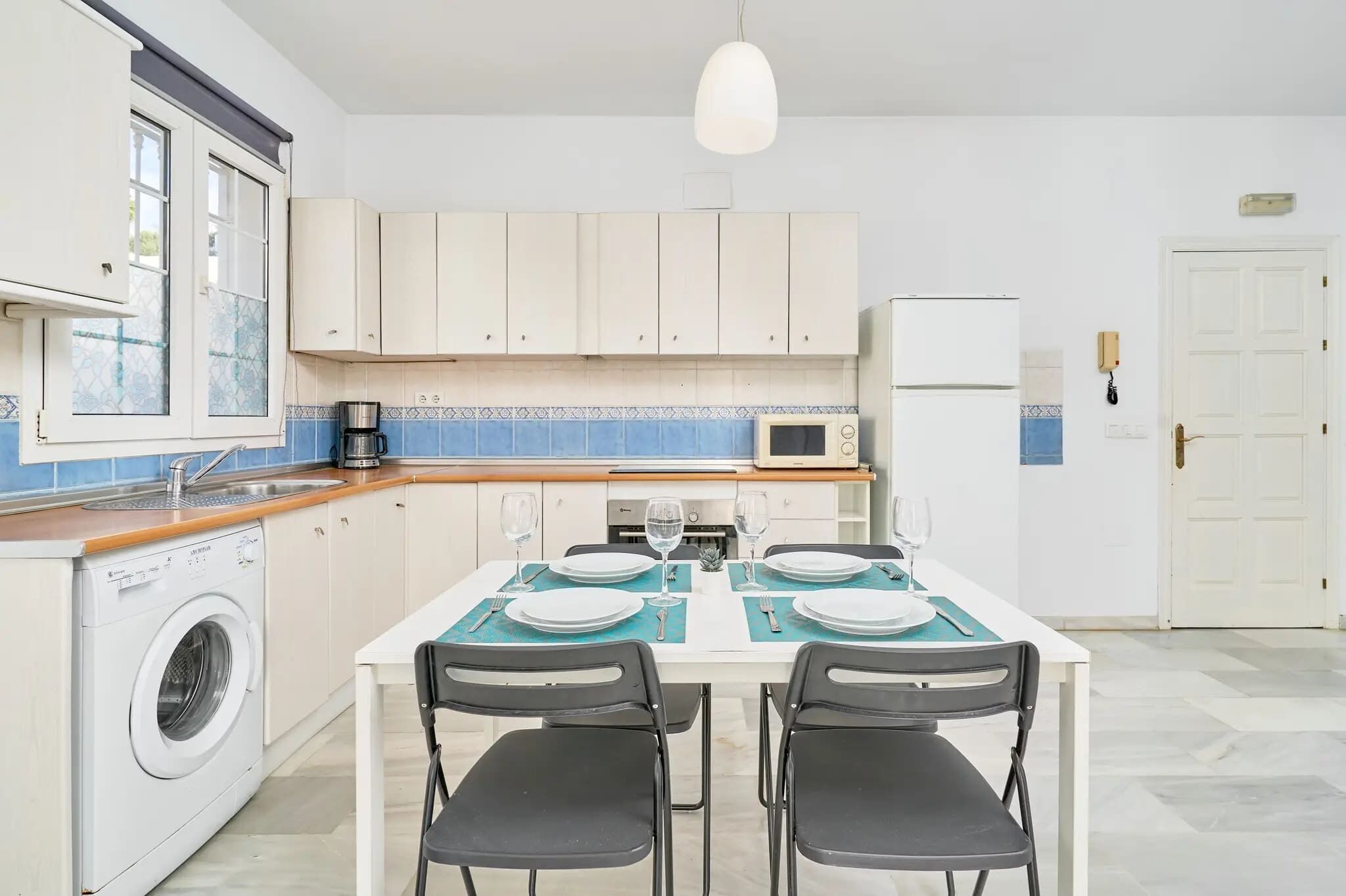 A kitchen with a washing machine, a microwave, and a dining table set for four.