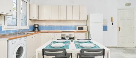 A kitchen with a washing machine, a microwave, and a dining table set for four.