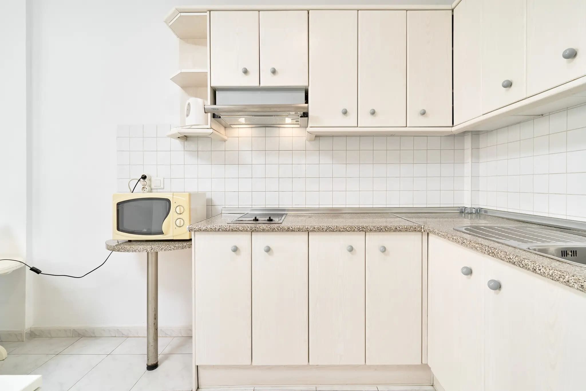 Una cocina con alacenas blancas, un microondas y un lavamanos de acero inoxidable.