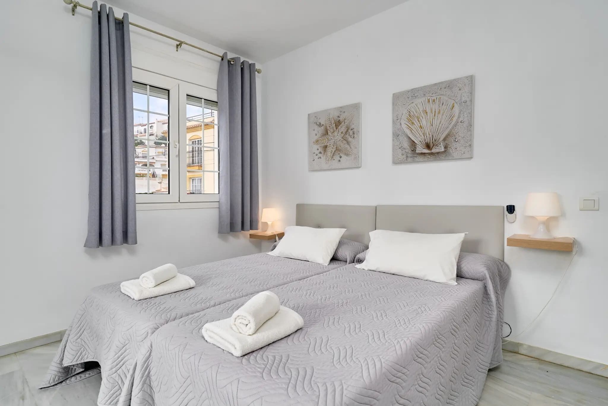 Une chambre d’hôtel avec un lit, deux oreillers, une table de chevet avec une lampe et des œuvres d’art accrochées au mur.