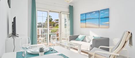 Ein modernes Wohnzimmer mit Essbereich, einer Couch, einem Liegesessel und einem Balkon mit Meerblick.